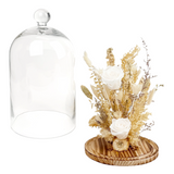 Clear glass cloche with wooden base featuring dried flowers and white roses on a white background