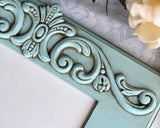 A robin's egg blue wood photo frame with a scroll embellishment at the top, designed to hold a 5x7 picture.