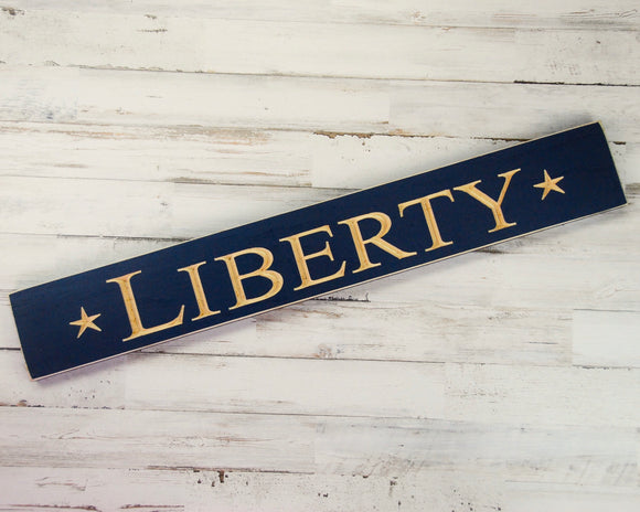 Liberty, Americana, Fourth of July, Patriotic, Navy, Blue, Military, JaBella Designs Show of your patriotism this summer with this rustic wooden wall hanging. It features the word “Liberty” flanked by two stars, all of which are engraved onto a long board that has been painted and distressed in navy blue. This would make a great gift for a military-themed man cave or garage.  This item is proudly made in the USA.