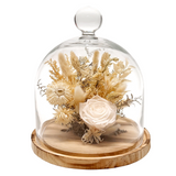 A dried flower arrangement under a clear glass dome cloche on a round wooden base, photographed against a plain white background.
