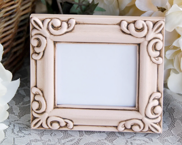 Decorative picture frame with intricate designs on a lace surface with flowers in the background
