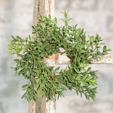 Green leafy wreath hanging on a wooden cross with a blurred background
