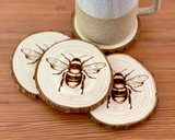 Engraved natural wood bumblebee coaster set
*Made to order*

Add cottagecore charm to a living room or bedroom with these coasters. They’re made from live edge California pine wood slices that are laser engraved with a honeybee illustration on one side. They are unfinished and smell quite nice.&nbsp;

Materials:
Wood

Dimensions:
3/4" thick 4" diameter