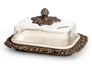 Decorative butter dish with glass cover and ornate bronze base on a white background
