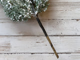 Faux greenery branch with white berries on a wooden surface