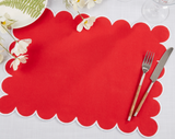 Red scalloped placemat with silverware on a white surface with flowers.