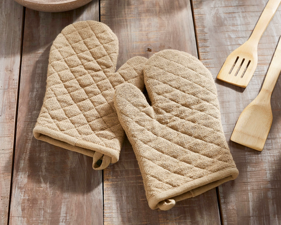 Pair of beige quilted oven mitts on a wooden surface with wooden utensils.