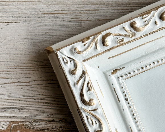 Decorative white frame with gold accents on a wooden surface
