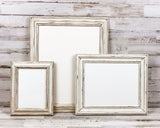Three distressed white picture frames of different sizes arranged on a rustic whitewashed wood surface against a matching wood plank background.
