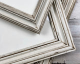 Distressed white wood picture frames with a weathered, rustic finish, stacked on a light gray wood-textured surface.