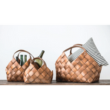 Three woven baskets with handles on a wooden surface against a white background