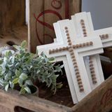 Decorative wooden cross with beads on a rustic wooden surface with a plant.