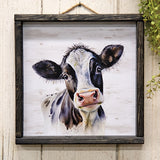 Black and white cow artwork, Cow print, JaBella Designs The print is a decorative wooden print with a distressed white background held inside of a chunky wooden box frame with a black finish and natural wood grain. The print features a black and white cow portrait, making it the perfect farmhouse touch for the home year-round. Display this print freestanding, propped, or on a wall using the jute hanger at the top. This item is proudly made in the USA.