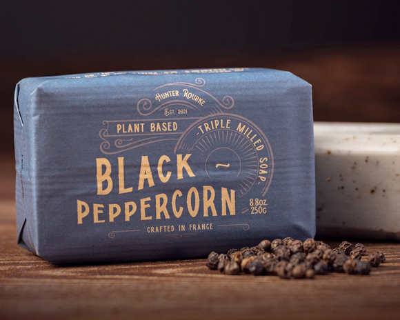 Bar of black peppercorn soap with packaging on a wooden surface