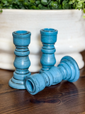 Three blue candle holders on a wooden surface with a blurred plant pot in the background.