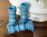 Three blue candle holders on a wooden surface with a white vase in the background.