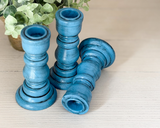 Three blue candle holders on a light surface with a plant in the background