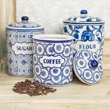 Set of blue and white ceramic canisters labeled 'Sugar', 'Coffee', and 'Flour' on a wooden surface.