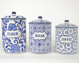 Set of three blue and white ceramic canisters labeled 'Flour', 'Sugar', and 'Coffee' on a white background.