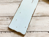 Handcrafted wooden wall cross painted in antique white with coffee brown distressing, featuring a handmade rustic burlap flower attached to the center.