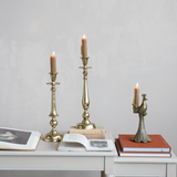 Three candle holders with candles on a table against a gray wall