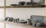 Ceramic tableware with floral patterns on wooden shelves against a white wall.