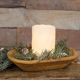 Candle in a wooden bowl with greenery against a rustic wooden background