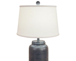 Bold yet refined, this handcrafted fibercast table lamp features a cylindrical base with subtle horizontal ridge detailing in a deep distressed charcoal finish. The textured surface adds depth and modern sophistication, while the neutral dark tone makes it a versatile statement piece for contemporary, rustic, or transitional interiors. Finished with a crisp white linen shade and a coordinating charcoal finial, it provides both style and substance to any room.

This item is proudly made in the USA.
