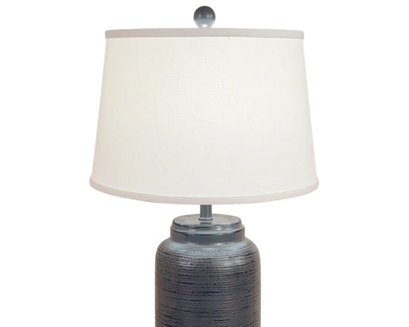 Bold yet refined, this handcrafted fibercast table lamp features a cylindrical base with subtle horizontal ridge detailing in a deep distressed charcoal finish. The textured surface adds depth and modern sophistication, while the neutral dark tone makes it a versatile statement piece for contemporary, rustic, or transitional interiors. Finished with a crisp white linen shade and a coordinating charcoal finial, it provides both style and substance to any room.

This item is proudly made in the USA.
