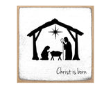 Square wall art print featuring a black nativity silhouette with a star and the words 'Christ is born' on a textured white background, framed by a tan border.