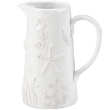 White ceramic pitcher with embossed sea-themed design on a white background