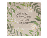 A greenery and floral motif surrounds the saying, "Stay close to people who feel like sunshine," on this painted wood plate, which features shades of taupe, ivory, and green. It will look great in a cottagecore-inspired collection. This particular plate is designed by artist Michelle Kildow.