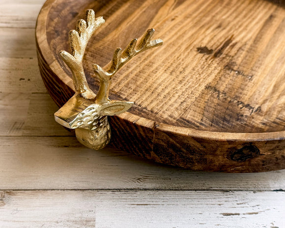 Wooden tray with a gold deer head ornament on a wooden surface