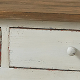 Close-up of a distressed white painted wooden cabinet drawer with a small round white knob and a brown wood top edge.