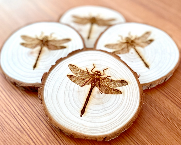 Wooden coasters with dragonfly designs on a wooden surface