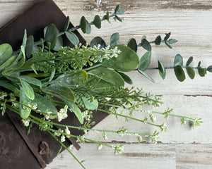 This decorative floral spray features a flexible green-wrapped stem. The spray is filled with lush branches of dark eucalyptus greenery alongside stems of white baby’s breath blooms. This spray is a beautifully addition to an artificial arrangement and would also work well in a wreath. Whether used in country cottage wedding centerpieces or holiday decorations, these sprays are perfect for your next event.  This spray is sold individually.  Materials: Artificial greenery  Dimensions: 19" long