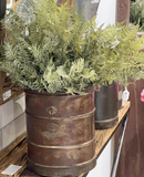 Artificial ferns in a rustic metal container on a wooden shelf.