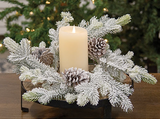 Decorative arrangement with a candle surrounded by frosted branches and pinecones on a wooden surface.