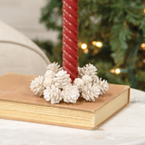 Red candle on a book with white pinecones against a blurred Christmas tree background
