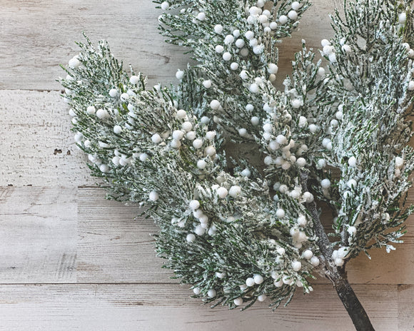 Decorative branch with green leaves and white berries on a wooden surface