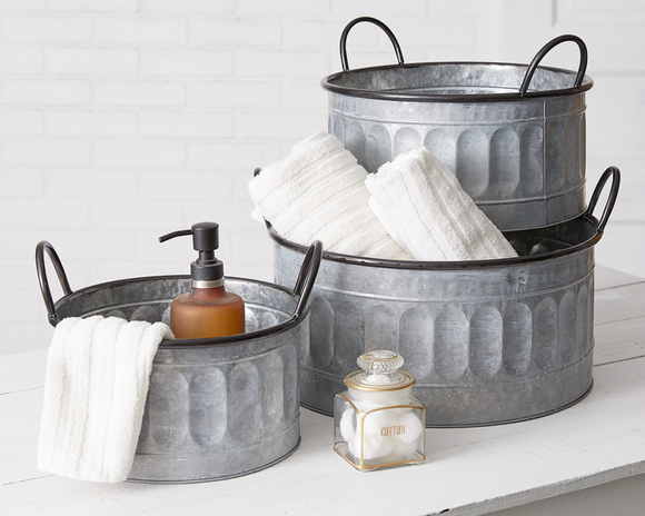 Set of three galvanized metal tubs with towels and a soap dispenser on a white surface.