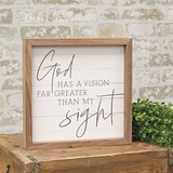 Wooden framed sign with 'God has a vision far greater than my sight' text on a stone wall background.