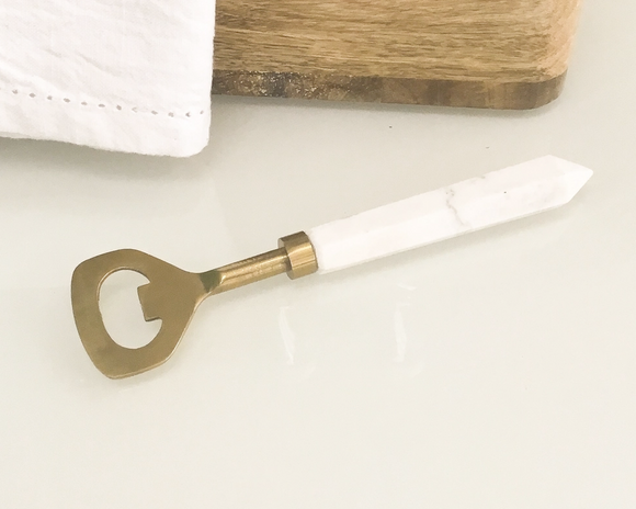 Bottle opener with white handle and brass cap on a light surface