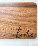 Wooden cutting board with 'It's so good to be home' text on a white background