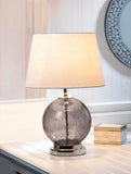 Table lamp with a textured glass base on a surface, with a decorative wall clock in the background.