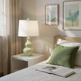 Bedroom with a lamp on a nightstand, open book, and green pillow.