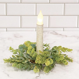 Flickering candle in a decorative holder with greenery on a marble surface.