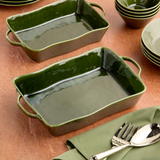 Green ceramic baking dishes on a wooden surface with silverware and napkins.