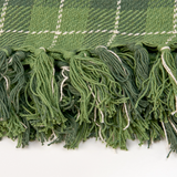 Close-up of a green plaid fabric with tassels on a white background