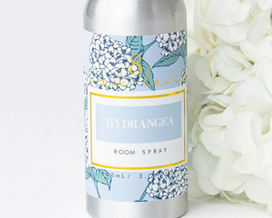 Room spray bottle with floral label next to white flowers on a light background